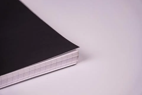 Closed black notebook with grid interior, positioned diagonally on a light gr Stock Photos