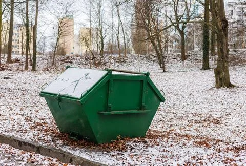 Closed green garbage collection container on the snow-covered foliage of th.. Stock Photos