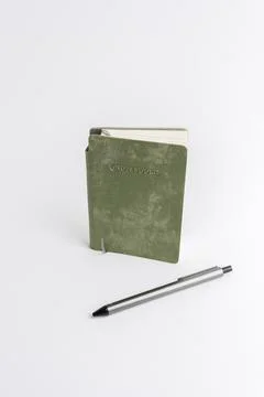 Closed green notebook standing vertically with a pen lying beside it isolat.. Stock Photos