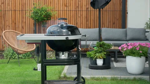 A closed kettle charcoal grill steams on a modern backyard patio terrace Stockbeeldmateriaal 340164377