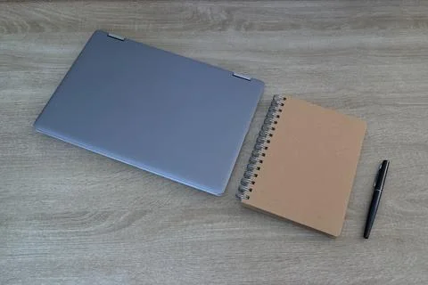 Closed laptop computer with kraft notebook and black pen on wooden desk, en.. 写真素材