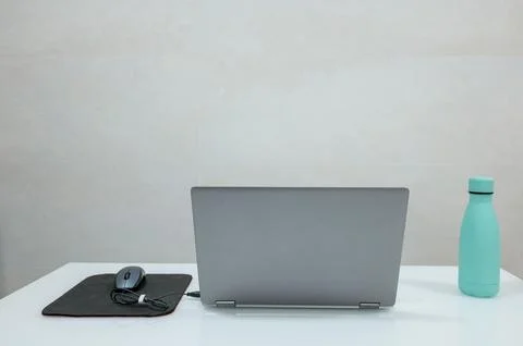 A closed laptop, wireless mouse, and water bottle on a white desk. 写真素材