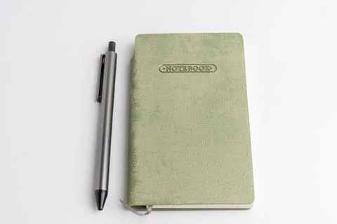 Closed light green cover notebook with a grey pen resting on it isolated on.. Stock Photos