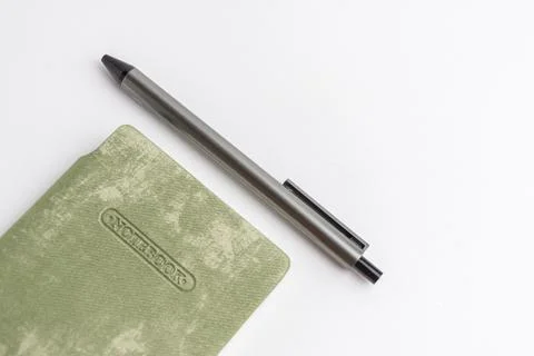 Closed light green cover notebook with a grey pen resting on it isolated on.. Stock Photos