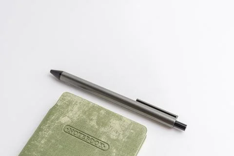 Closed light green cover notebook with a grey pen resting on it isolated on.. Stock Photos