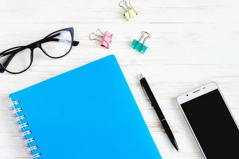 Closed notebook, pen, glasses, mobile phone, a cup of coffee on a white woode Stock Photos