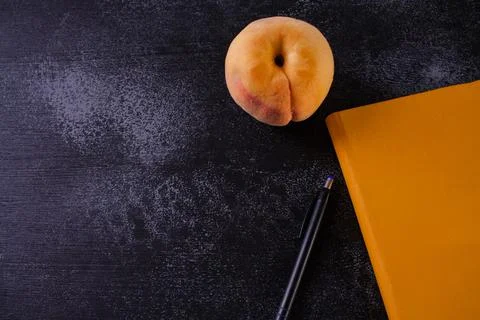 Closed orange notebook, pen and peach Stock Photos