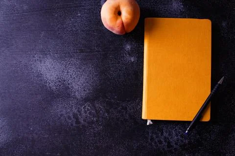 Closed orange notebook, pen and peach Stock Photos