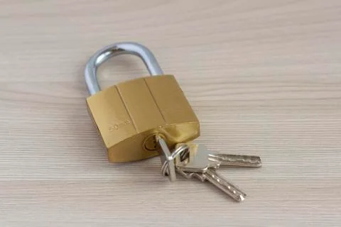 Closed padlock with keys in the keyhole on a light wooden background. Stock Photos