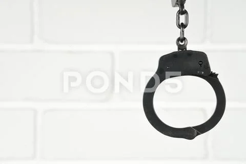 Closed police handcuffs against a white brick wall Stock Photos
