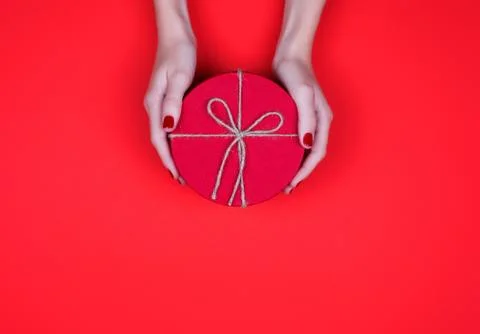 Closed red round gift box in woman hand on red background. Top view. Gift for Stock Photos