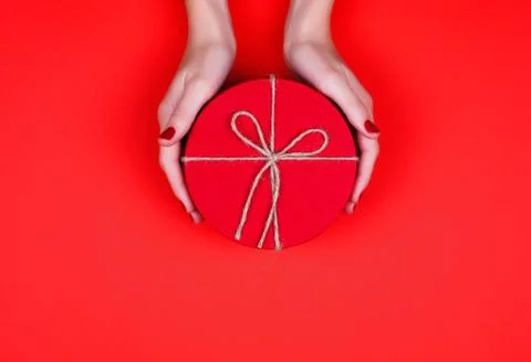 Closed red round gift box in woman hand on red background. Top view. Gift for Stock Photos