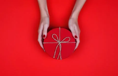 Closed red round gift box in woman hand on red background. Top view. Gift for Stock Photos