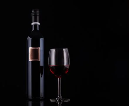 Closed red wine bottle with empty label and glass of wine on black background Stock Photos