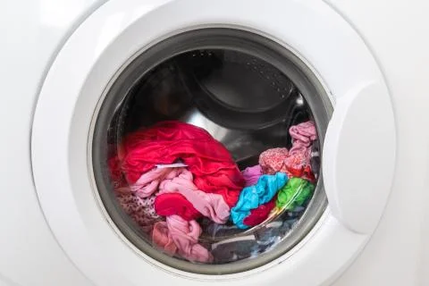 Closed round washing machine door with rotating garments inside. Focus in the Stock Photos
