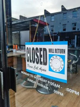 Closed sign on cafe door with empty seating inside and city reflections Stock Photos