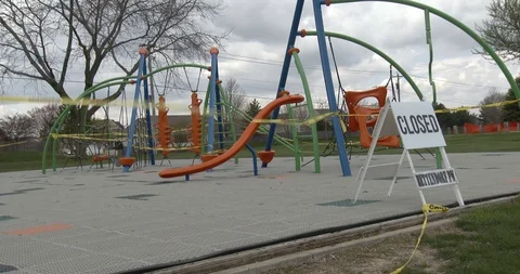 CLOSED sign in front of a Playground with Caution Tape Blowing in the Wind Stock Footage 128783344
