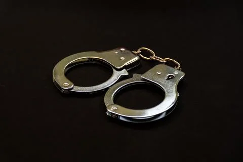 Closed silver handcuffs placed on a dark background representing crime preven Stock Photos