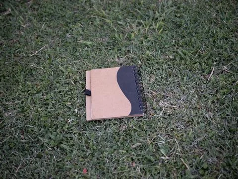 Closed spiral notebook lying on grass outdoors Stock Photos