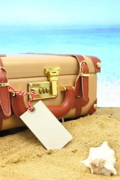 Closed suitcase with empty tag on tropical beach background Stock Photos