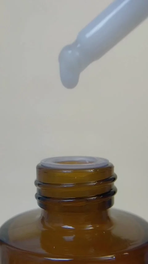 Closed up view of a dropper dripping a milky white liquid into the bottle. Vídeo Stock 335296759