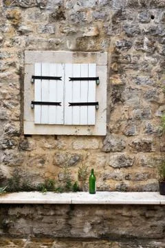 Closed window shutters in a stone wall with a green wine bottle Stock Photos