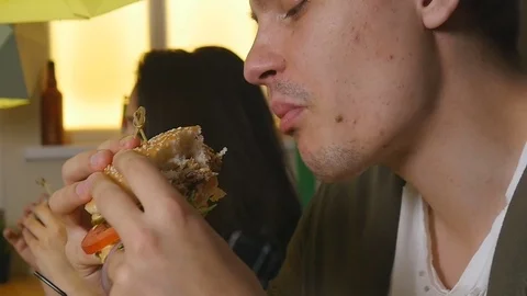 Closer up man bites and eats burger at a cafe Stock Footage 76162742