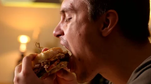 Closer up man bites and eats burger at a cafe Stock Footage 76167665