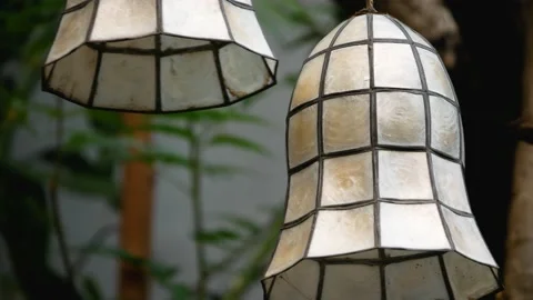 A closeup of 2 "Capiz" shell lanterns swaying in the wind outdoors, in a garden. Stock Footage 150109629