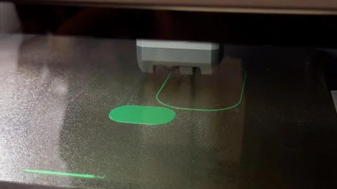 Closeup of 3D printer nozzle depositing green filament onto textured build plate Stock-Footage 346558155