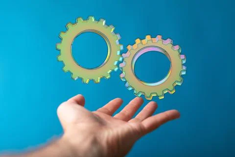 A closeup of a 3D rendered gears floating on a man's hand isolated on a blue  스톡 사진