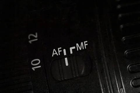 Closeup of the AF MF switch on the camera lens. Dark background. Photos