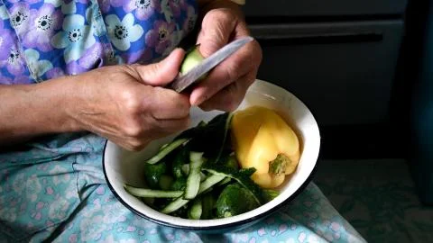 Closeup of aged female hands cutting raw cucumbers