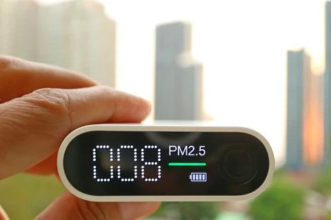 Closeup of an air quality sensor in hand against group of high buildings 스톡 사진