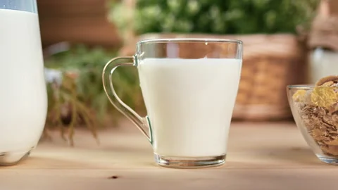Closeup appetizing fresh milk in mug and jug with muesli in bowl on wooden Stock Footage 165866703
