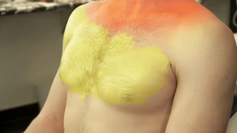 Closeup of art makeup master covering man's body with yellow color with the Stock Footage 73539952