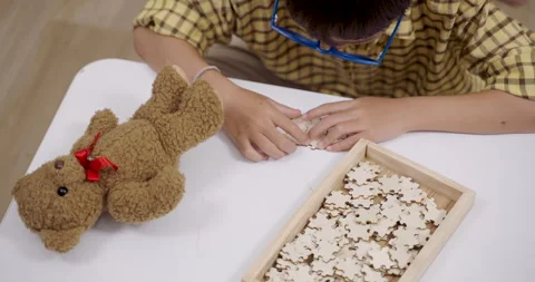 Closeup of asian boy with ADHD using fingers to solve puzzle while teddy bear Stock Footage 313741008