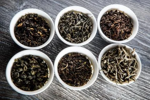 Closeup assorted tea leaves in six white small round vessels on gray wooden t 写真素材