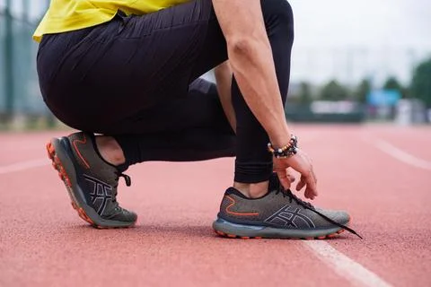 Closeup of athlete man taking a break from training, tying his sneaker laces at Stock Photos