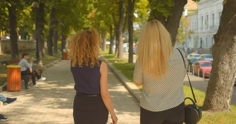 Closeup back view portrait of two female friends walking in park outdoors Stock Footage 114894413