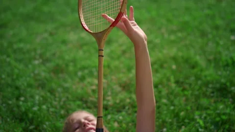Closeup badminton racket in hands of smiling joyful girl lying on blanket. Stock Footage 170518121