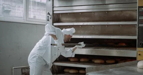 Closeup baker take off the baking bread from oven and unloaded on the shelves Stock Photos