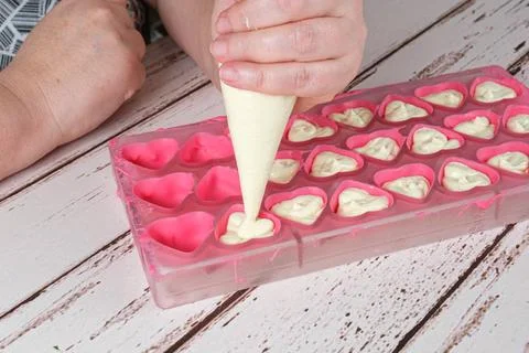 Closeup of baker using a confectioner's nozzle to fill chocolates with white  Stock Photos