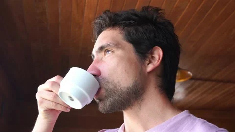 Closeup of bearded white man drinking coffee in white cup in morning looking at Stock-Footage 199509810
