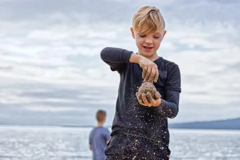 A closeup of a beautiful young boy on the beach, playing with sand. Stock Photos