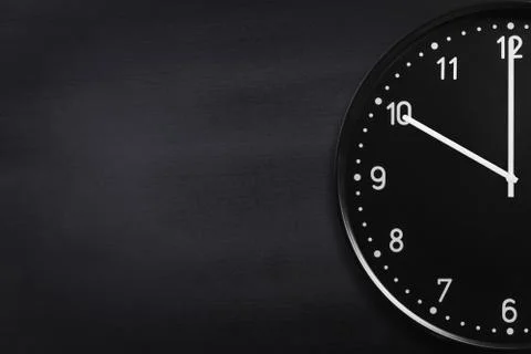 Closeup of black wall clock on black chalkboard background Stock Photos