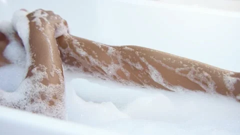 Closeup of a black woman's arm caressing herself in a white foam bathtub in slow Stock Footage 231634541