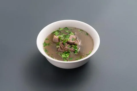 Closeup of bone broth with beef meat and parsley in bowl on grey background Foto stock