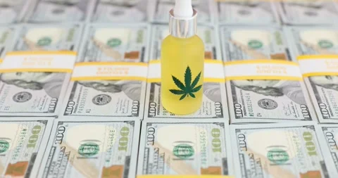 Closeup of bottle of CBD oil with green hemp leaf on it with hundred dollar Stock Footage 281159041