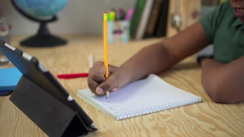 Closeup of boy writing in notebook and sitting at table with tablet during home Stock Footage 163818788